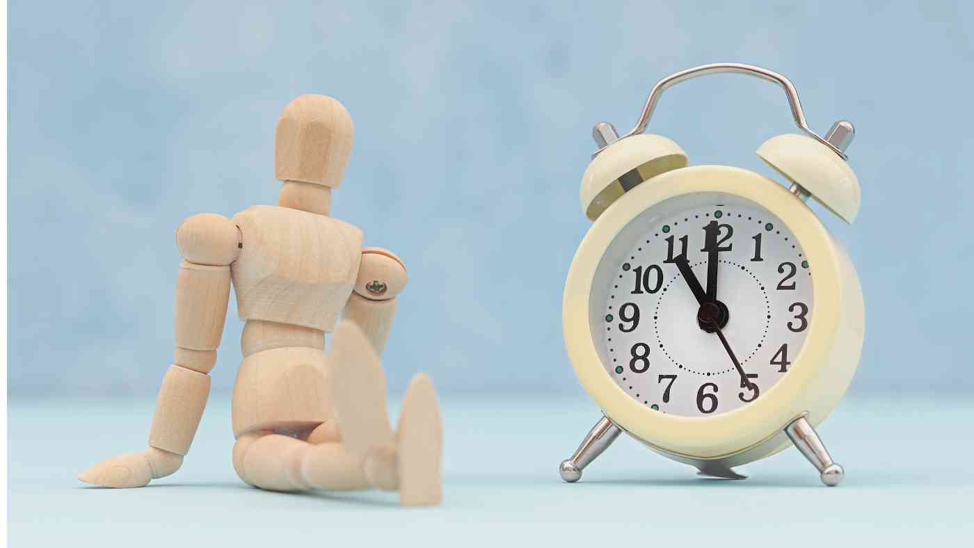 Wooden mannequin sitting beside a yellow alarm clock, symbolizing time management and legal strategies related to Texas DWI penalties.